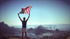 Athlete stands holding an American flag waving in slow motion at a bright overlook of the city skyline of Rio de Janeiro, Brazil