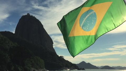 Brazilian flag flying in front of scenic sunrise view of Sugarloaf Mountain and Guanabara Bay at Praia Vermelha, Red Beach, in Urca, Rio de Janeiro, Brazil