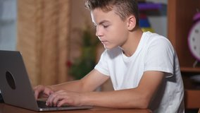 Cute teen boy working on laptop computer or watching video in internet