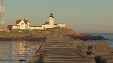 Mid shot view of Eastern Point Lighthouse on Cape Ann with light beam flashing and boulders located at the northeastern tip of Gloucester harbor Massachusetts USA

