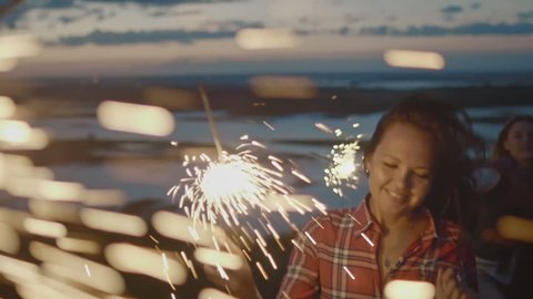 Smiling young woman dancing on a high hill with sparkler at sunset in slow motion