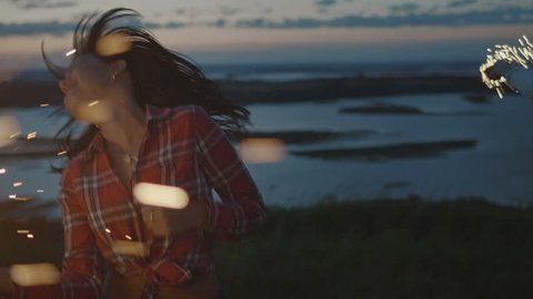 Beautiful young woman dancing on a high hill with sparkler at sunset in slow motion