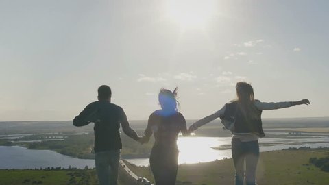 Group Of Friends Hold Hands on a high hill at sunset And Run Away From Camera ,Slow Motion