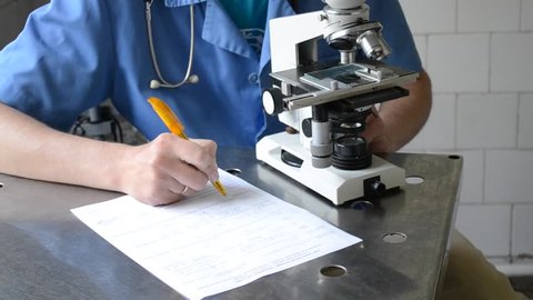 doctor looking into a microscope and writing on paper
