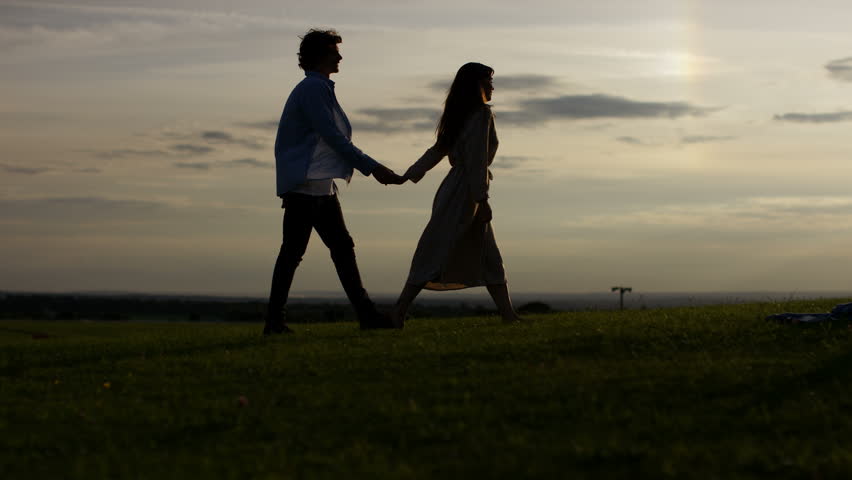4K Silhouette man proposes at sunset to his girlfriend and she accepts, in slow motion