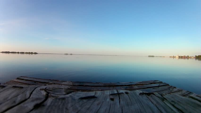 Two men jump from a wooden pier in the water throwing up shoes
