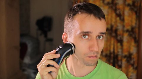 Hndsome young man shaving with electric razor. Electric shaver in living room