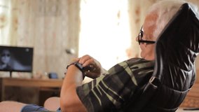 Senior man sits with smart clock in a leather chair near the house TV. A man looks at the message by a smart watches - Powered by Shutterstock - Get 15% off with code: PIKWIZARD15
