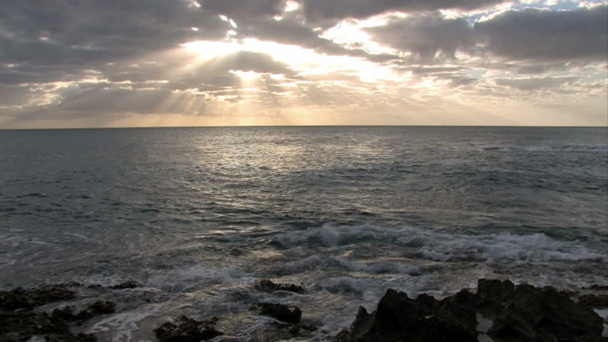 Tropical sunset over ocean in Hawaii. Tropical scene with ocean, palm trees and surf. Bright colorful sky. Sun rays streaming down to Pacific ocean.