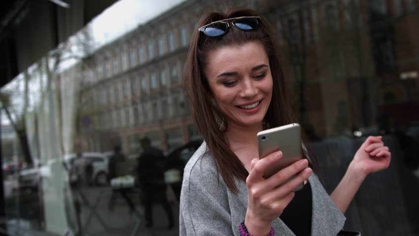 Delighted young woman reading asms on her mobile phone smiling with excitement at the good news as she stands outdoors Royalty-Free Stock Footage #18055270