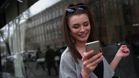 Delighted young woman reading asms on her mobile phone smiling with excitement at the good news as she stands outdoors