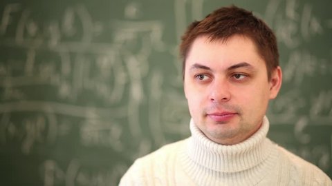 Face of man in sweater close-up turning to blackboard.