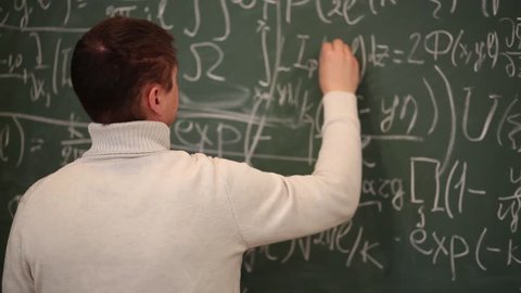 Back of man in sweater correcting symbols in equations on blackboard.
