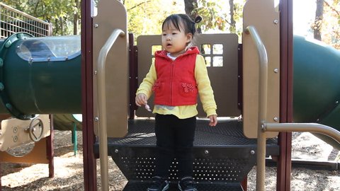 Beautiful Asian Baby Toddler Girl in Red Vest on Playground Set