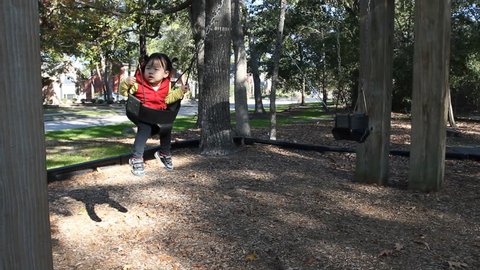 Beautiful Asian Baby Toddler Girl in Red Vest Swinging on Swing