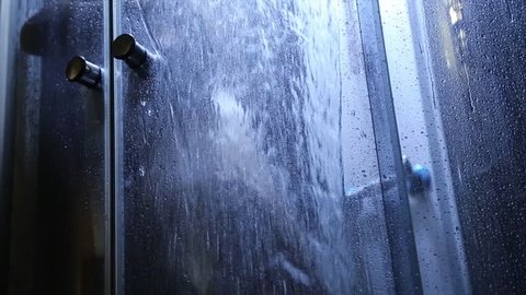 Showering woman silhouette blurred by the transparent door. woman taking shower and washing her body with shower gel behind sliding glass door covered with water drops
