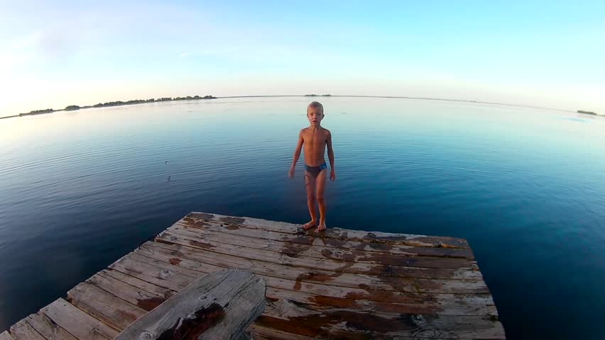 Kid jumps off a wooden dock into the water . Slow motion Royalty-Free Stock Footage #18064474