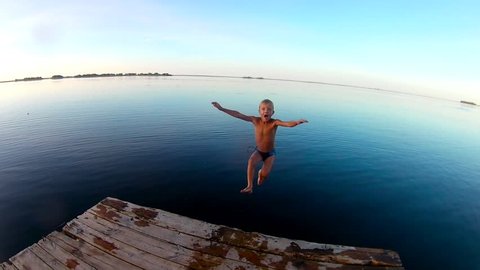 Kid jumps off a wooden dock into the water . Slow motion
