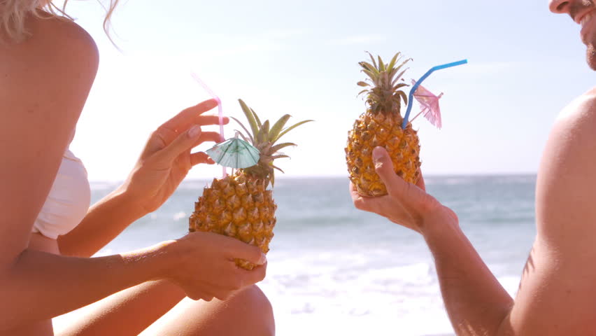 Smiling couple drinking in a pineapple on the beach
