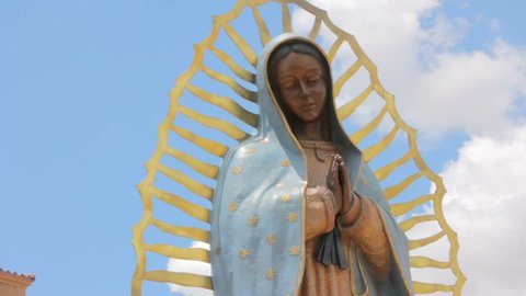 Low angle shot of a statue of the Virgin of Guadalupe. The religious icon symbolizes peace and serenity. The blue sky behind the patron Saint of Mexico gives a heavenly feeling of salvation.