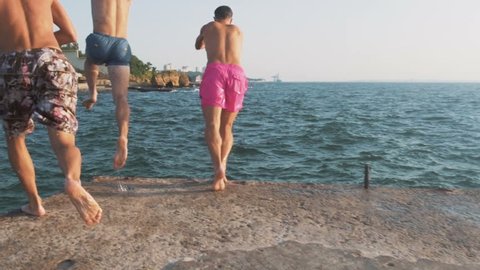 Group of friends running and jumping off sea pier in the water, slow motion