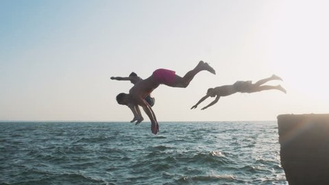 Group of friends running and jumping off sea pier in the water, slow motion
