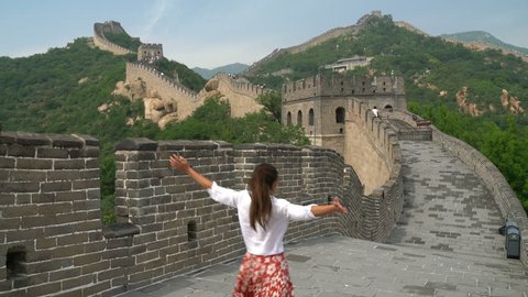 Happy cheerful joyful tourist woman at Great Wall of China having fun on travel smiling laughing and dancing during vacation trip in Asia. Girl visiting and sightseeing Chinese destination in Badaling