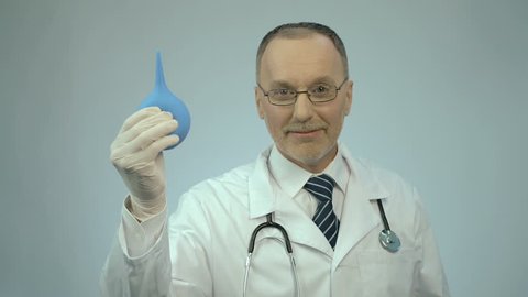 Happy smiled proctology doctor showing rubber syringe and looking at camera