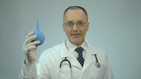Funny doctor pressing on rectal syringe with smile on face, proctologist joking