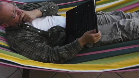 a man lies on a hammock and works with his laptop