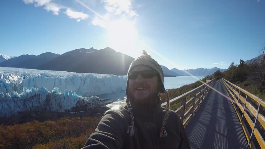 Smiling Happy Man With a Beard Shoots Himself and Glacier and the Picturesque Nature Around on a Clear Sunny Day