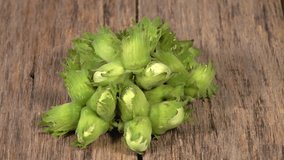 Rotation of unripe green filbert nut heap on desk of old wood board in soft light. 4K UHD footage 3840x2160. Beauty of natural fresh and old texture.
