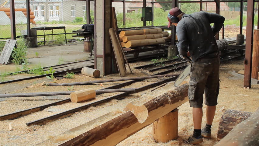Man cuts off beam chainsaw for future home. Construction works with a wooden structure