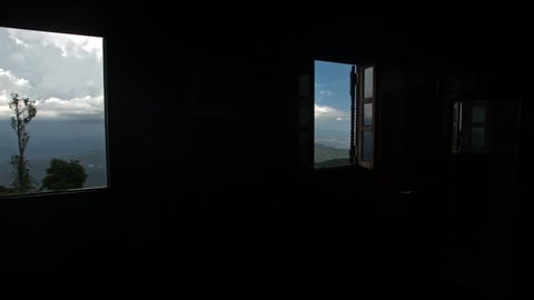 camera moves away from hilly country landscape against cloudy blue sky through open window to room