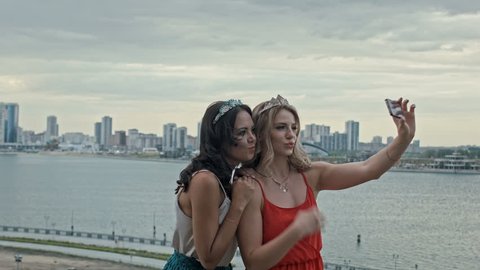Two young beautiful girls having fun and making selfie on high hill over the city