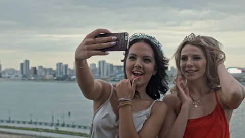 Two young beautiful girls making selfie on high hill over the city