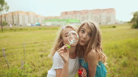 Two girls on a city background blow soap bubbles