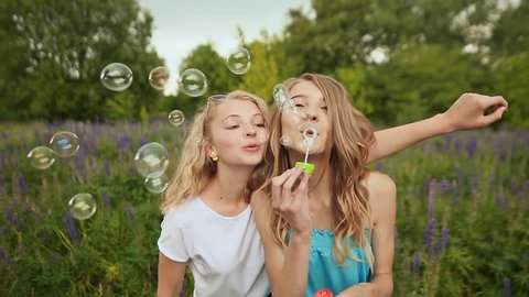 Beautiful joyful teenagers laughing and blowing soap bubbles in spring park. Girlfriends outdoor. Friendship
