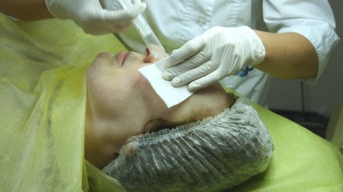 Old woman lies and getting eyelash makeup at beauty salon. Applying Permanent Make up on eyelash. Hands of beautician are preparing the skin for the procedure or cleaning after the procedure