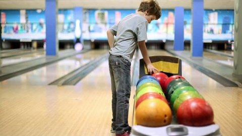 Little boy takes bowling ball and throws it to beat skittles