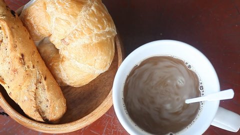 Coffee pouring into cup and bread on a wooden table. Breakfast