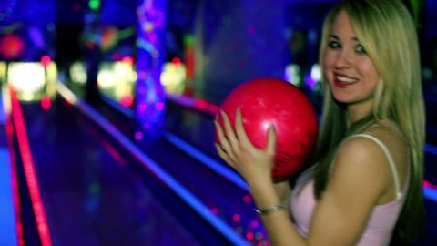 Young girl stands and smiles with bowling ball and then throws it to beat skittles