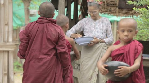 BAGAN, MYANMAR, July 4, 2016: Old Burmese woman giving alms to novice Buddhist monks in Bagan, Myanmar (Burma)