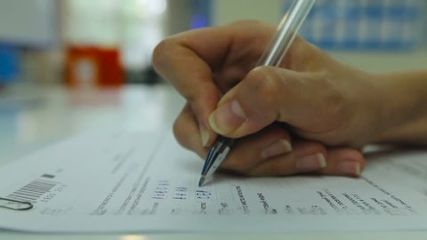 Zoom in Woman's Hand Neatly Complete a Form. Woman Writes With a Pen. Man Goes in the Background. Closeup