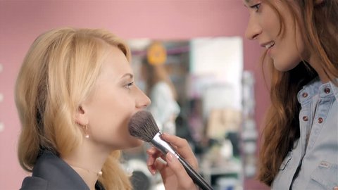 Make up artist doing professional make up of young woman, brush in stylist hands.