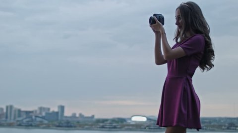 Attractive young woman fashion model in purple party dress photographs outdoor in front of skyline, close up