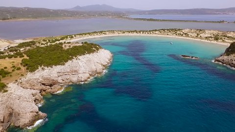 Aerial view from the popular Voidokilia beach in Peloponnese, Greece. A half-moon-shaped beach surrounded by vivid water in an unrealistic way.  Low angle panning sideways.