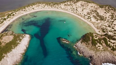 Aerial view from the popular Voidokilia beach in Peloponnese, Greece. A half-moon-shaped beach surrounded by vivid water in an unrealistic way. Forward motion.