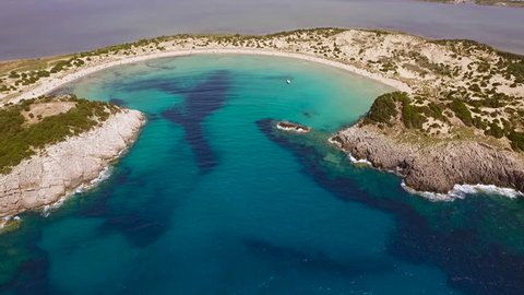Aerial view from the popular Voidokilia beach in Peloponnese, Greece. A half-moon-shaped beach surrounded by vivid water in an unrealistic way. Slow rising motion.
