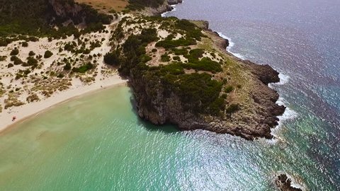 Aerial view from the popular Voidokilia beach in Peloponnese, Greece. A half-moon-shaped beach surrounded by vivid water in an unrealistic way. Camera rotates along the coastline. 